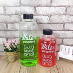 Two water bottles with black lids, one green and one red, on a wooden surface with a white brick wall background.