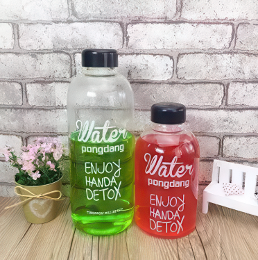 Two water bottles with black lids, one green and one red, on a wooden surface with a white brick wall background.
