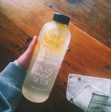 Hand holding a bottle labeled 'Enjoy Handy Detox' on a wooden surface