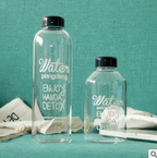 Two clear glass water bottles with black lids on a teal background