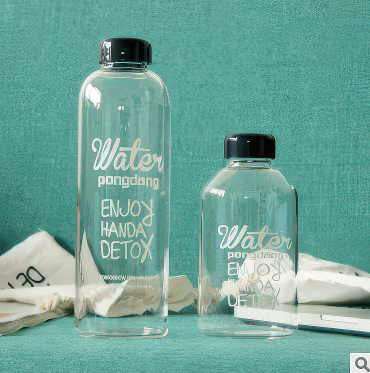 Two clear glass water bottles with black lids on a teal background